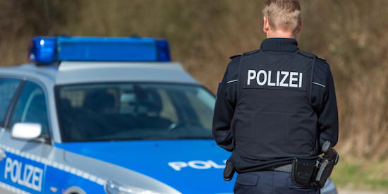 Ein Polizist steht vor einem blauen Polizeiauto