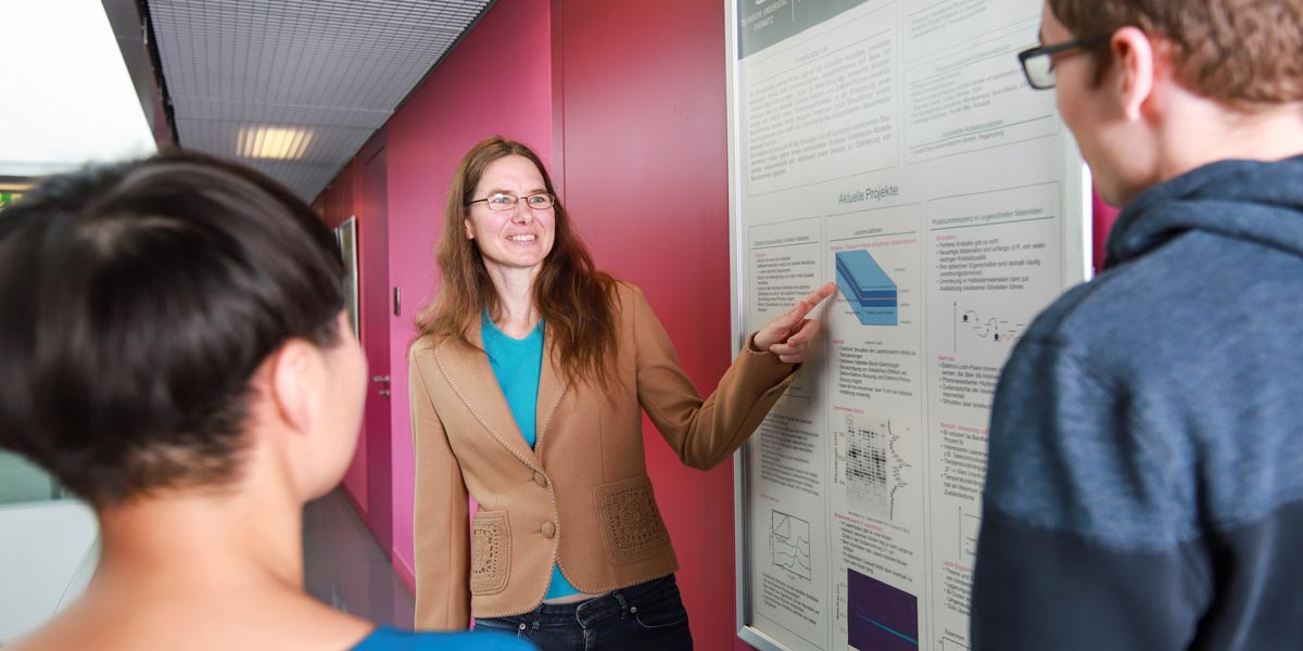 Dozentin erklärt Studierenden etwas an einem wissenschaftlichen Poster
